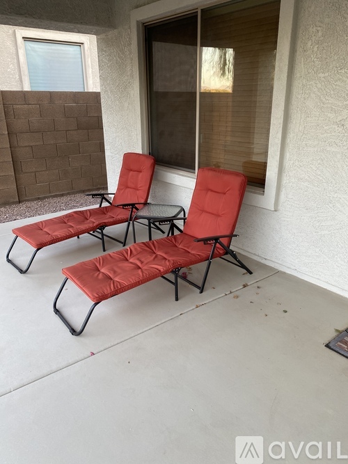 Two red chairs and a table are on a patio.