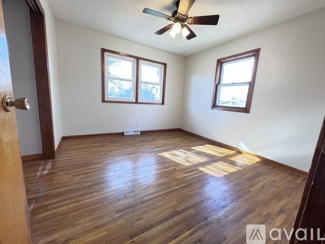 A room with wooden flooring and two windows.