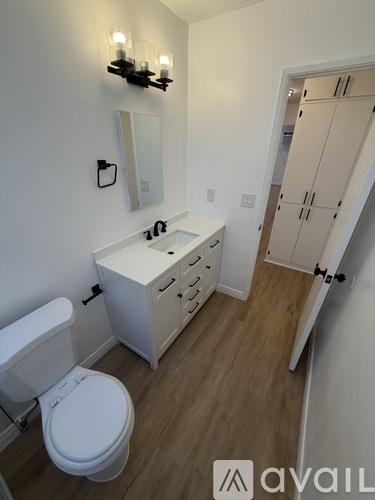 A white toilet sits in a small bathroom with a white cabinet and a white sink.