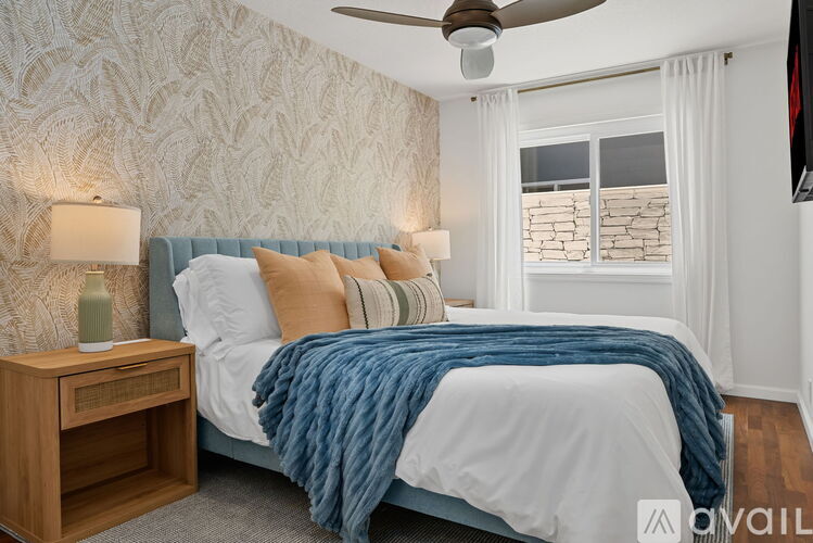 A bedroom with a bed, a ceiling fan, and a nightstand with a lamp.