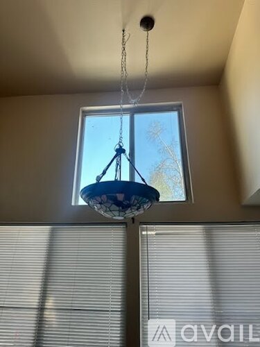 A hanging light fixture with a blue shade is suspended from a chain in a room with a window covered in blinds.