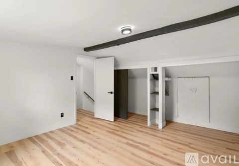 A room with a wooden floor and white walls, featuring a white door and a white cabinet.