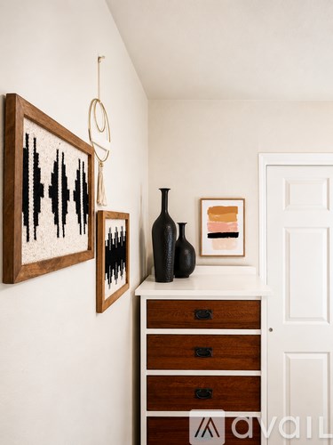 A black vase sits on a white shelf next to a framed picture and a hanging hoop.