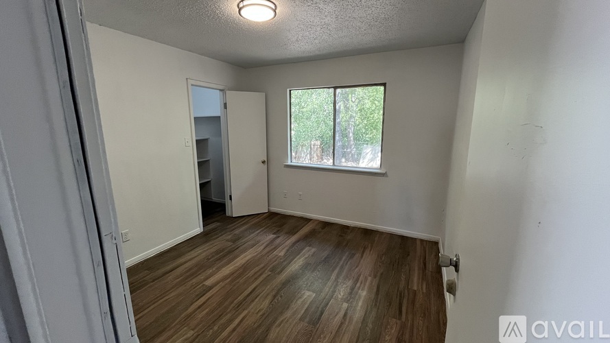 A room with wooden flooring and a window with a view of trees.