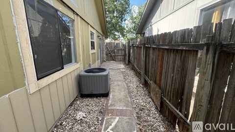 A narrow alley with a wooden fence on one side and a wall with a window and air conditioner on the other.