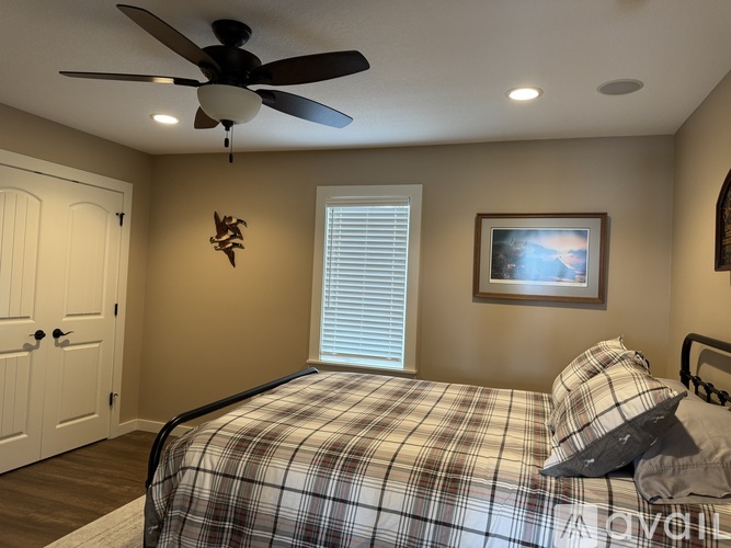 A bedroom with a bed, a ceiling fan, and a picture on the wall.