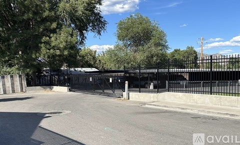A black fence surrounds a paved area with trees in the background.