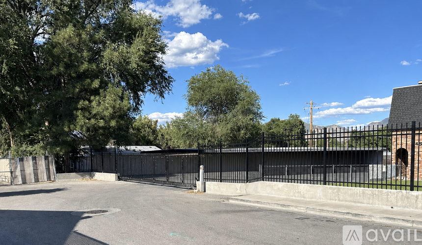 A black fence surrounds a paved area with trees and a building in the background.