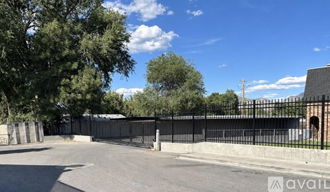 A black fence surrounds a paved area with trees and a building in the background.