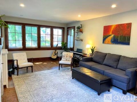 A living room with a grey couch, a white chair, a guitar, and a painting on the wall.