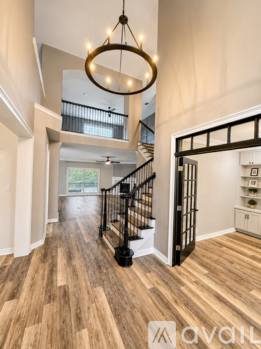 A large, well-lit room with wooden floors and a staircase with black railings.