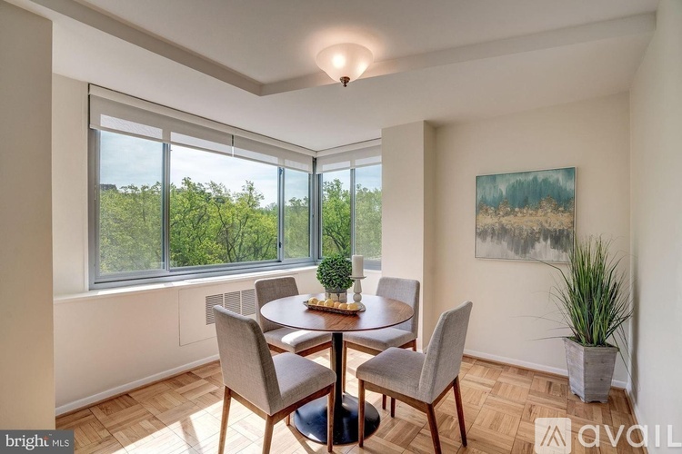 A dining room with a table set for four and a painting on the wall.