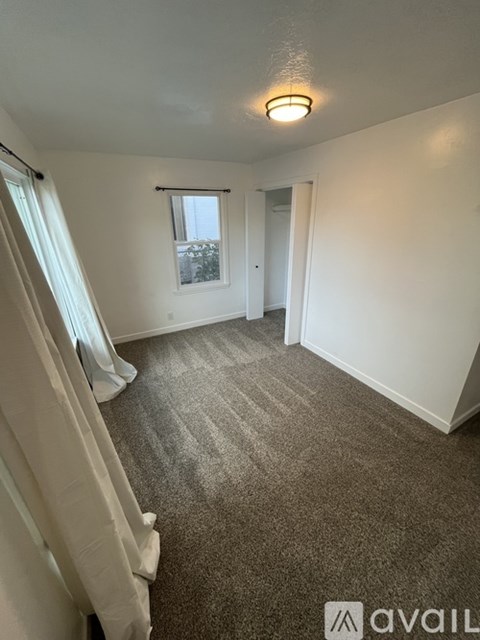 A carpeted room with a window and a door leading to another room.
