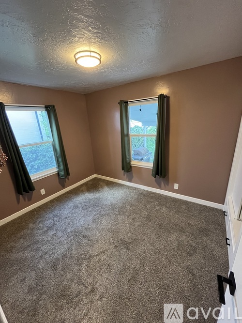 A room with a carpeted floor and two windows with curtains.