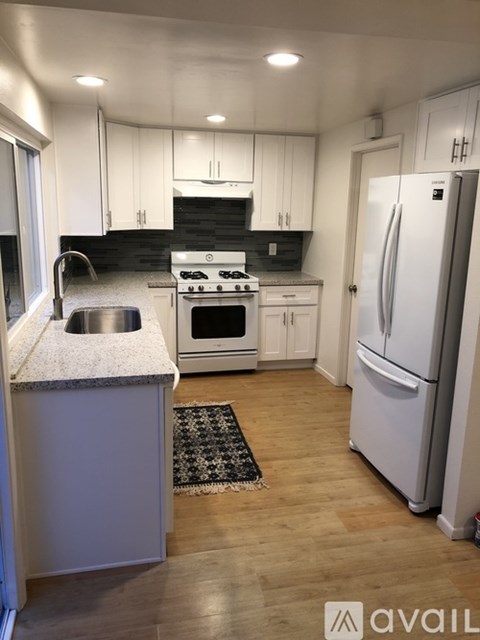 A kitchen with a white fridge and a black and white rug on the floor.