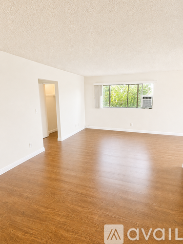 A room with wooden flooring and a window overlooking trees.