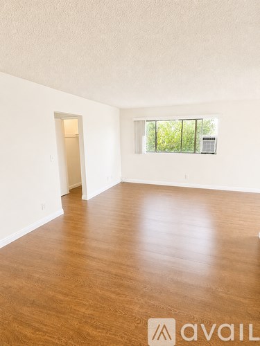 A room with wooden flooring and a window overlooking trees.