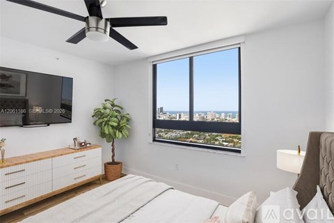 A bedroom with a large bed, a ceiling fan, and a view of the city through a window.