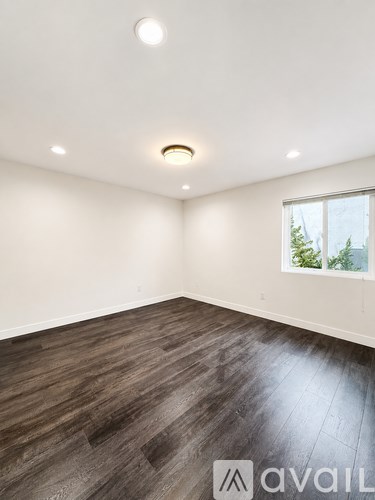 A room with wooden flooring and a window showing a view of trees outside.
