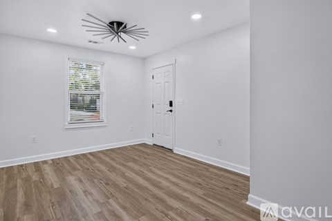 A room with a white door, a window with blinds, and a wooden floor.