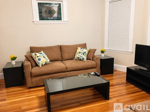 A living room with a brown couch, a glass coffee table, and a television.