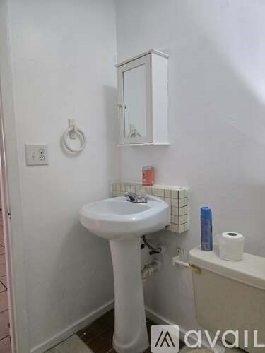 A white sink in a small bathroom with a toilet paper roll and a toothpaste tube on the counter.