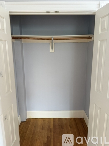A white closet with a wooden shelf and a white door.