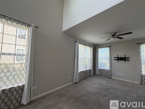 A spacious room with a ceiling fan and large windows with curtains.