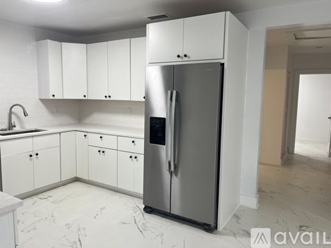 A kitchen with a refrigerator, cabinets, and a marble floor.