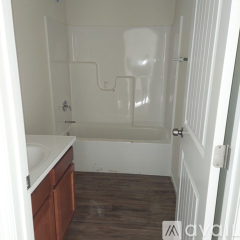 A small bathroom with a white tub and wooden floors.