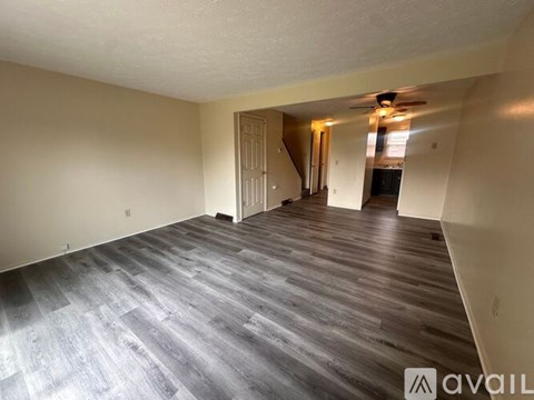 A spacious room with wooden flooring and a staircase in the background.