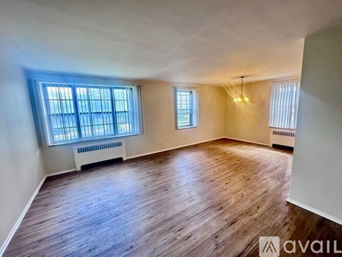 A spacious room with wooden flooring and two windows.