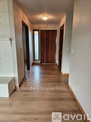 A hallway with wooden floors and white walls, with a door at the end.