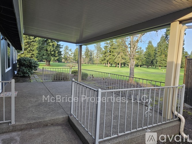 A patio with a metal railing and a view of a green lawn and trees.