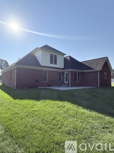 A house with a red brick exterior and a white trim is shown on a sunny day.