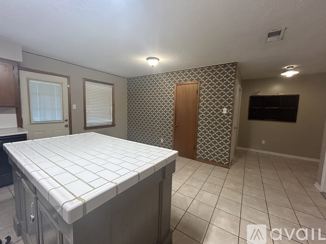 A kitchen with a white tile countertop and a patterned wallpapered wall.