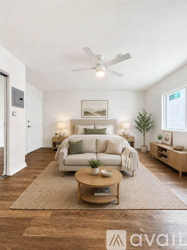 A well-lit, spacious bedroom with a large bed, a couch, a coffee table, and a small potted plant.
