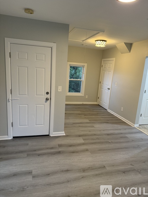 A room with a white door and a window with a view of trees outside.