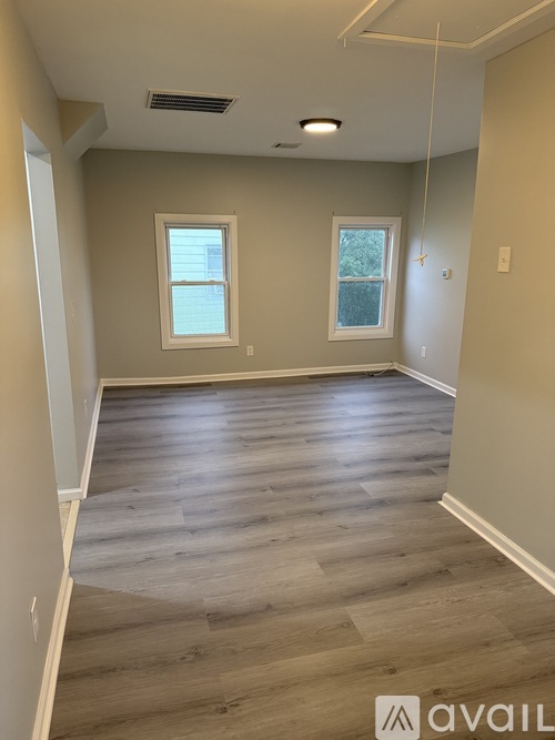 A room with wooden flooring and two windows.