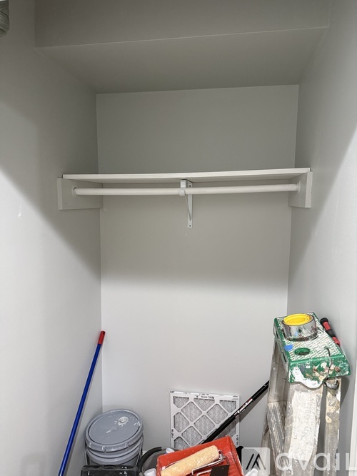 A white shelf with a broom and a red bucket on the floor.