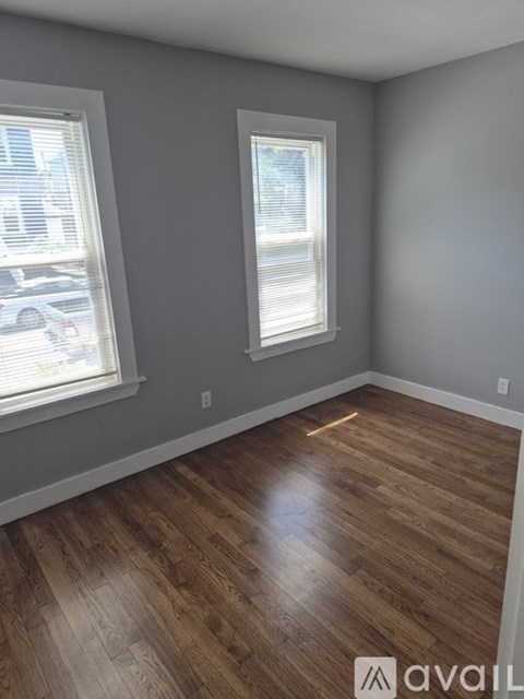 A room with wooden flooring and two windows.