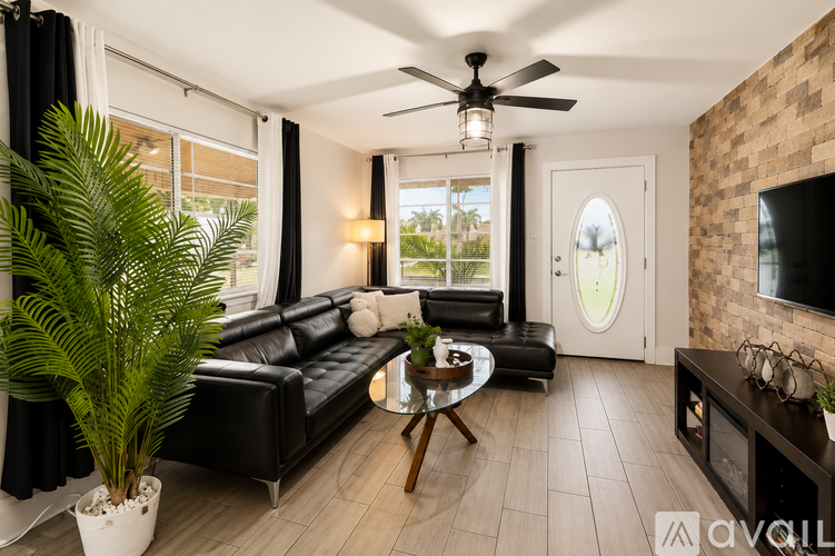 A living room with a black leather couch and a ceiling fan.