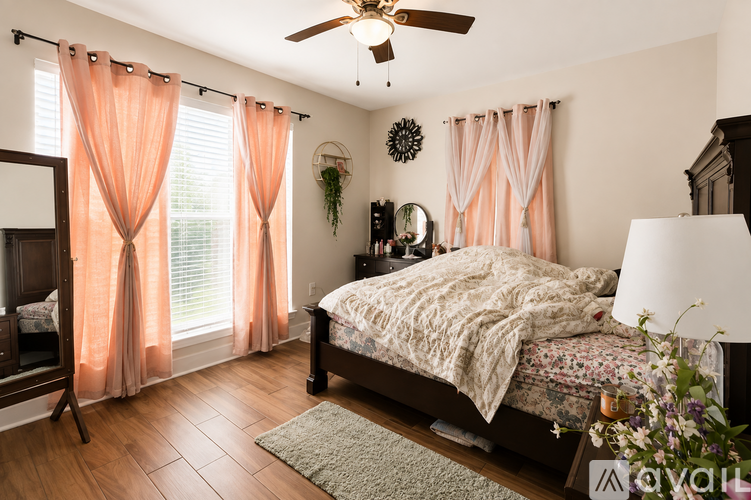 A bedroom with a bed, a dresser, a mirror, a ceiling fan, and a window with curtains.