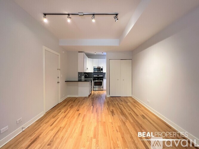 A spacious room with wooden flooring and a kitchen area in the background.