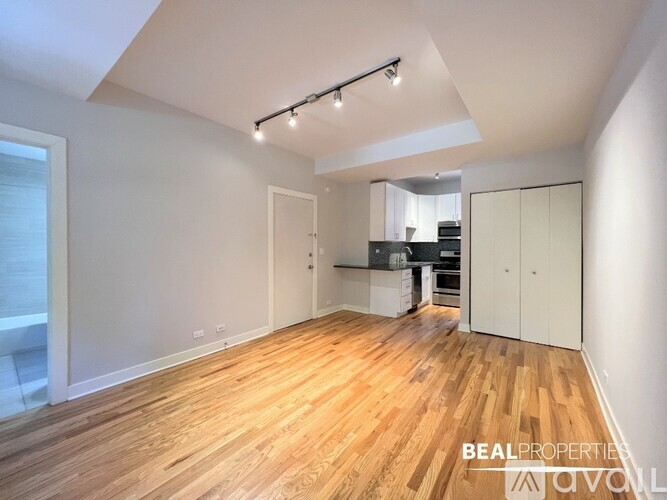 A spacious room with wooden flooring and a kitchen area in the background.