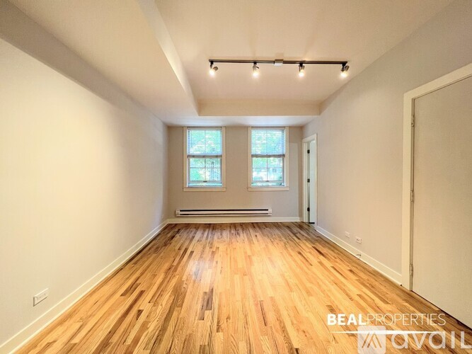 A spacious room with wooden flooring and two windows.