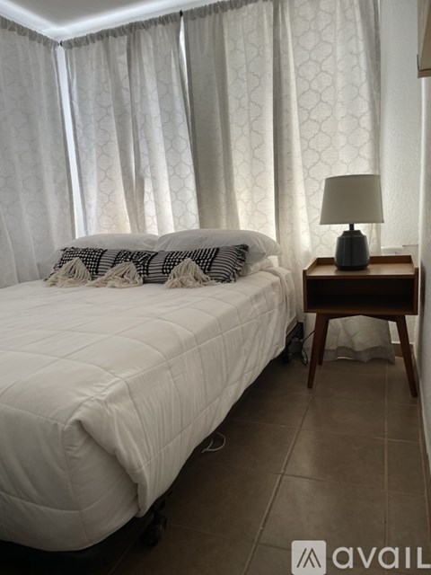 A bedroom with a white bed and a lamp on a wooden table.