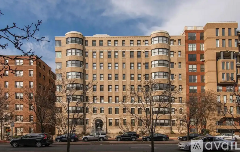 A large, multi-story building with a curved corner entrance is surrounded by parked cars.