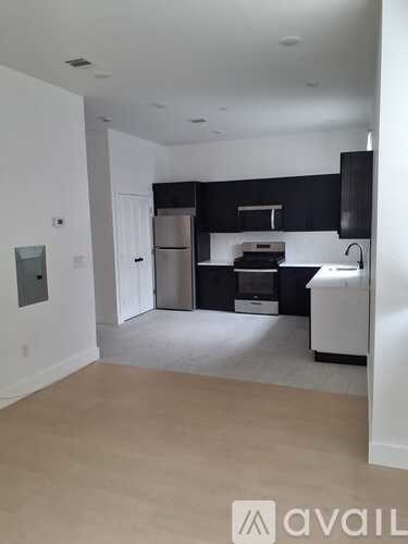 A kitchen with black cabinets and white appliances in a white room.