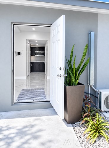 A doorway opens to a dark room with a plant on the other side.